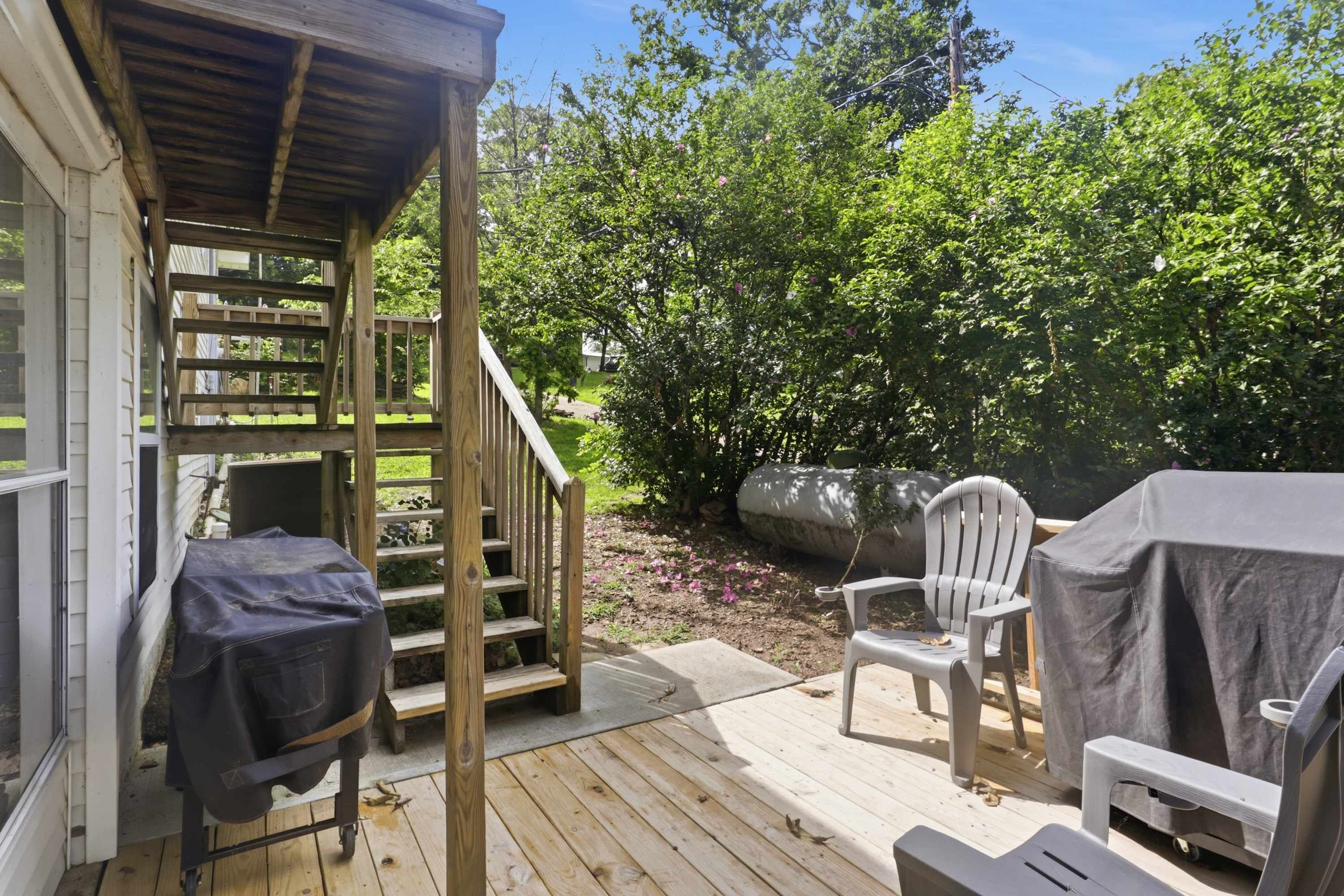 A wooden deck with outdoor furniture, a covered grill, and a staircase leading to a covered porch.