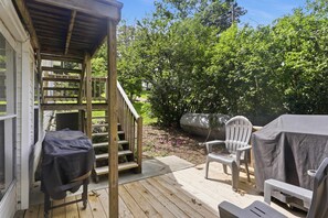A wooden deck with outdoor furniture, a covered grill, and a staircase leading to a covered porch.