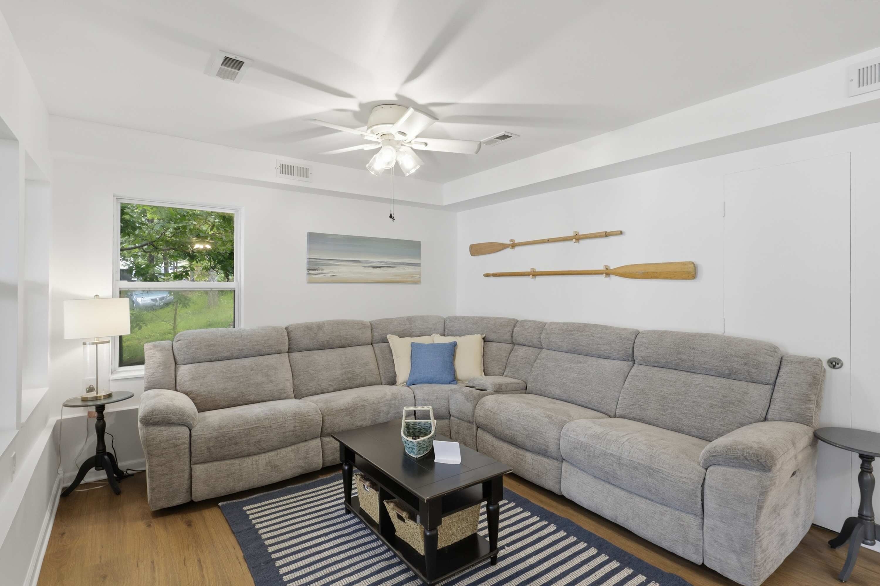 A living room with a sectional sofa, a small table, a ceiling fan, and two paddles on the wall.