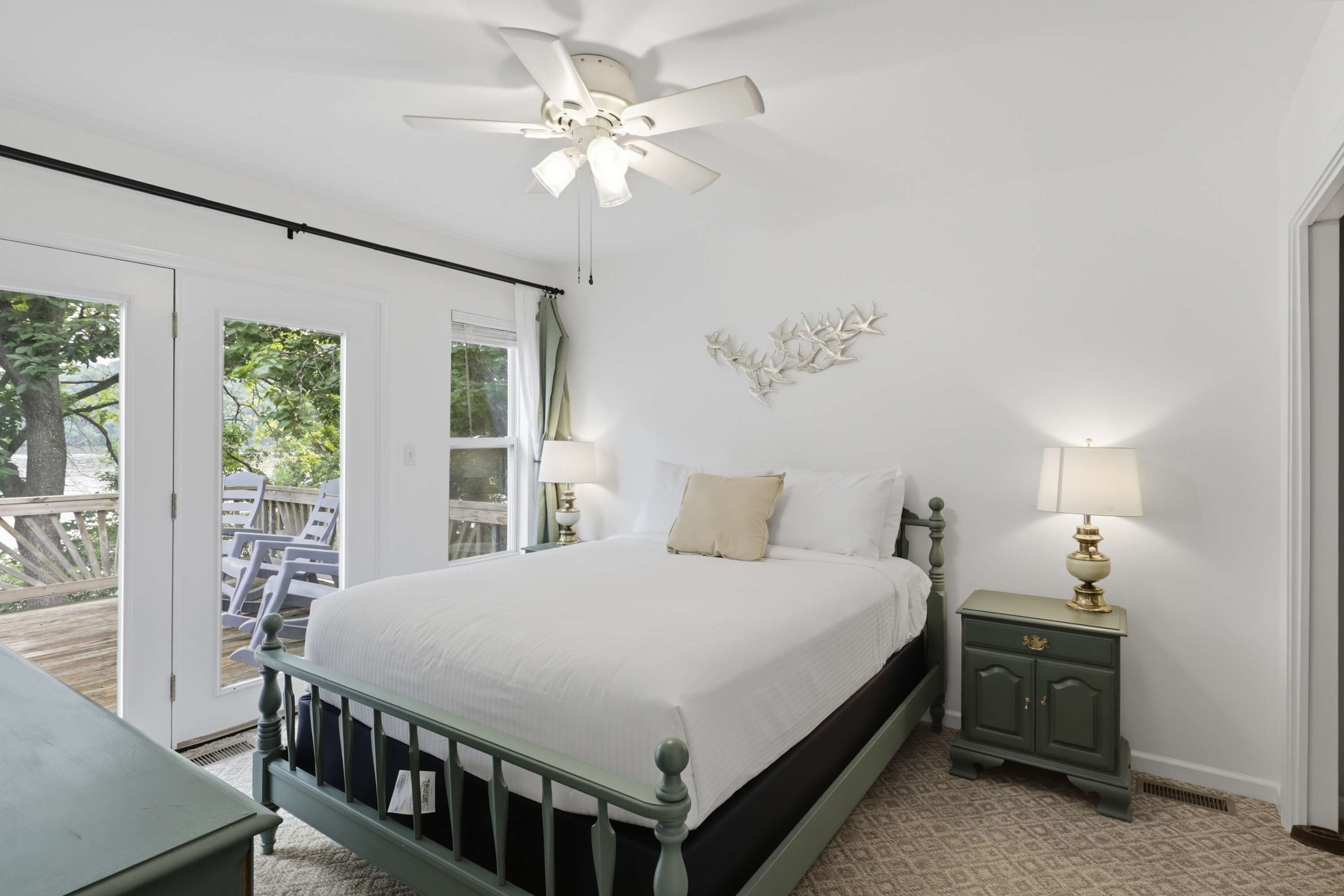 A bedroom with a bed, a nightstand, a ceiling fan, a window, and a door leading to an outdoor area.