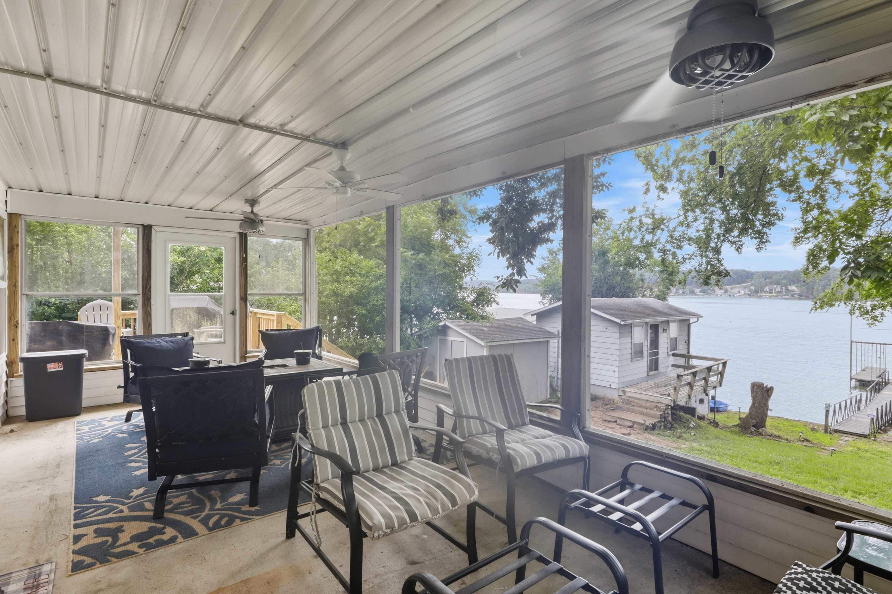 Un patio couvert avec vue sur un lac, des meubles d’extérieur et un espace barbecue.