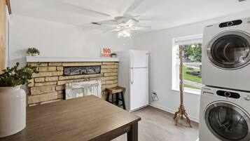 A laundry room with stacked washers and dryers, a ceiling fan, a refrigerator, and a window with a view of greenery.
