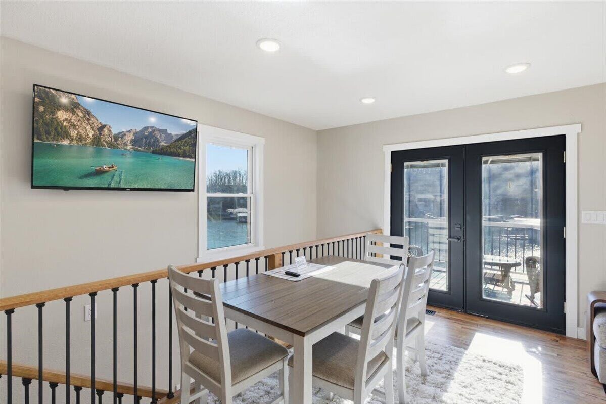 A dining area with a table and chairs, a television mounted on the wall, and a sliding glass door leading to an outdoor patio.