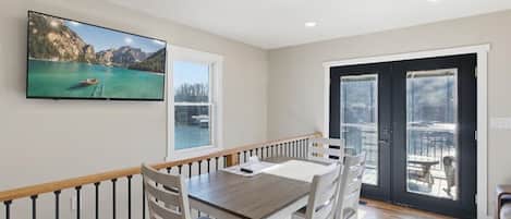 A dining area with a table and chairs, a television mounted on the wall, and a sliding glass door leading to an outdoor patio.
