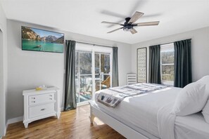 Ein Schlafzimmer mit Bett, Deckenventilator, Fernseher und einem Fenster mit Vorhängen.