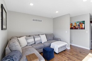 Ein modernes Wohnzimmer mit einem grauen Ecksofa, einem kleinen Hocker und einem Bild an der Wand.