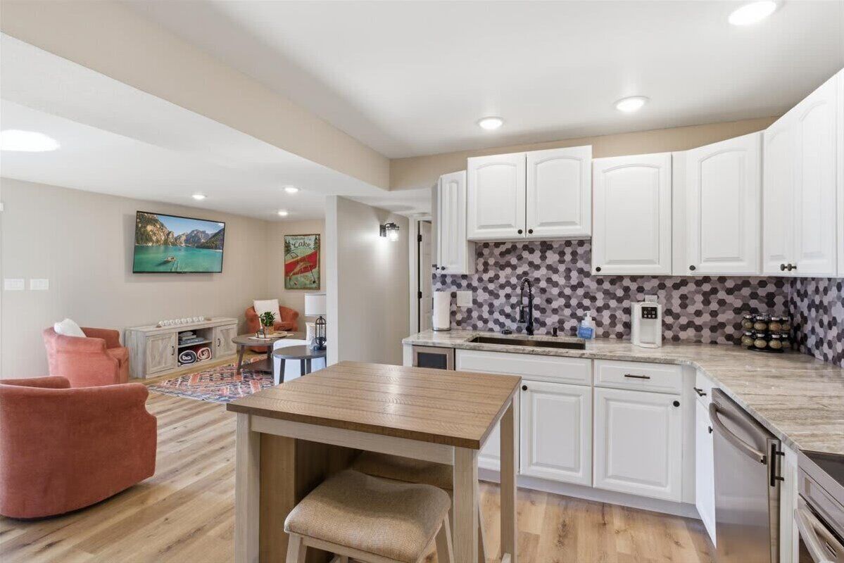 A modern kitchen with white cabinets, a marble countertop, and a dining area with a wooden table and chairs.