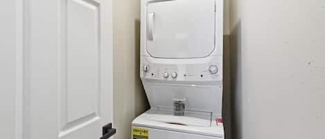 Une petite buanderie blanche, équipée d’un lave-linge et d’un sèche-linge à chargement frontal, d’une porte et d’une petite fenêtre.
