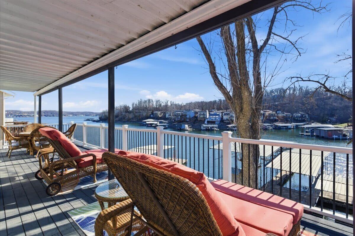 Une terrasse couverte, aménagée avec des meubles en osier, offrant une vue sur un port de plaisance.