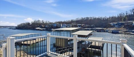 A waterfront property with docked boats, a wooden deck, and a view of the water and distant buildings.