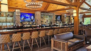 Un rústico espacio de bar con techo de madera, pilares de piedra y asientos de cuero.