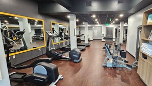 Un gimnasio con máquinas de cardio, equipo de levantamiento de pesas, espejos y un estante de madera con toallas dobladas.