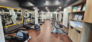Ein Fitnessraum mit Cardiogeräten, Gewichten, Spiegeln und einem Holzboden mit gefalteten Handtüchern.