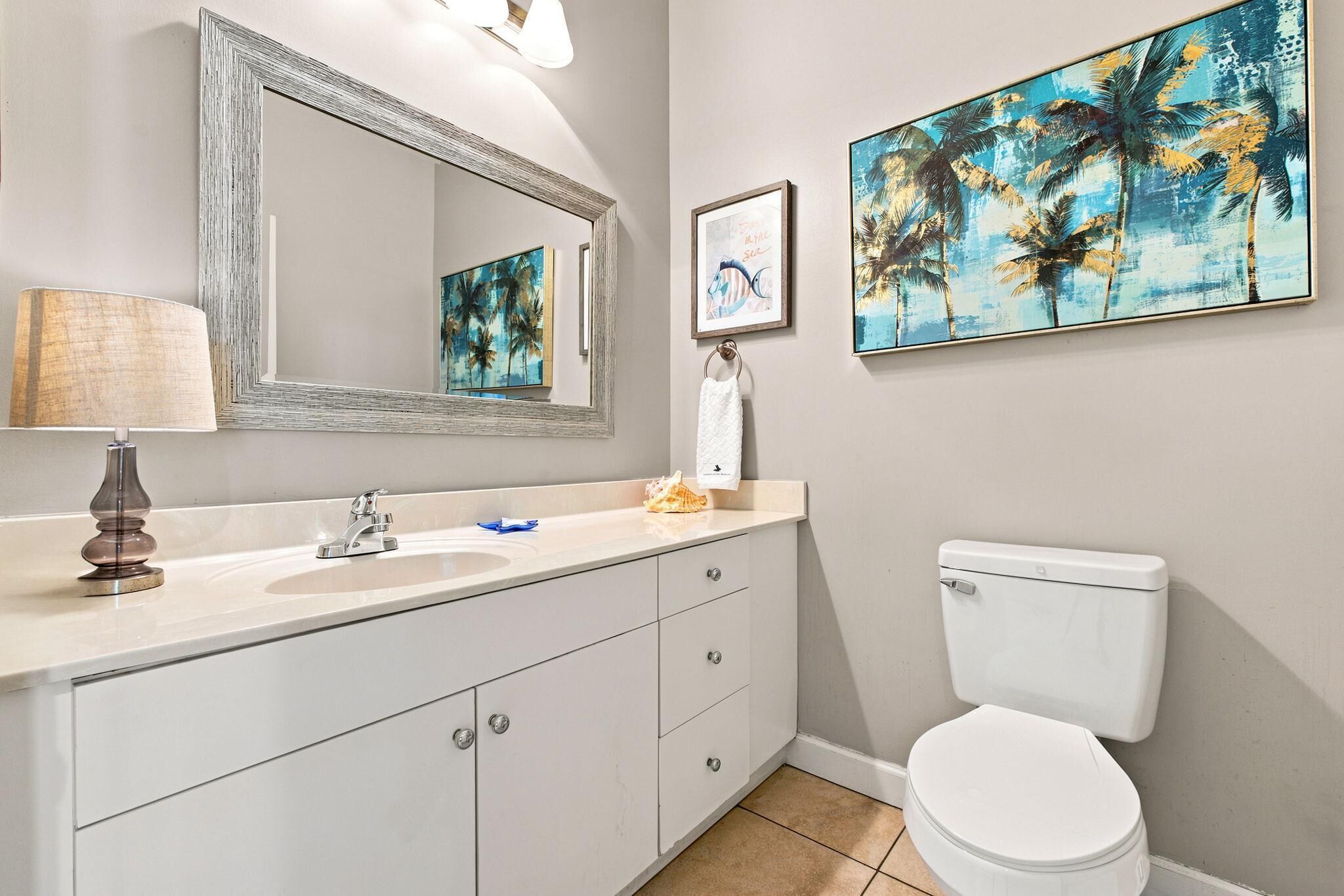 Een badkamer met een witte wastafel, spiegel en toilet. Twee kunstwerken hangen in lijsten aan de muur.