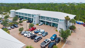 A multi-story building with a parking lot, surrounded by trees and a clear sky. - Villagio C241 (Pensacola)
