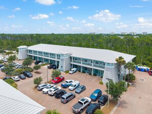 A multi-story building with a parking lot, surrounded by trees and a clear sky. - Villagio C241 (Pensacola)