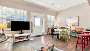 A living room with a television, sofa, and a dining area with chairs and a table. - Villagio C241 (Pensacola)