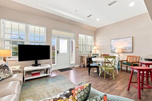 A living room with a television, sofa, and a dining area with chairs and a table. - Villagio C241 (Pensacola)