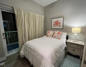 A bedroom with a bed, nightstand, lamp, and a window with curtains. - Villagio C241 (Pensacola)