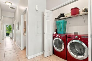 A laundry room with a red washing machine, a teal laundry basket, and a red bucket on a shelf. - Villagio C241 (Pensacola)