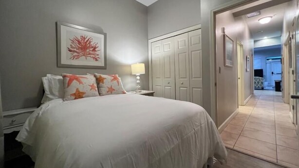 A hotel room with a bed, a nightstand, a lamp, a wardrobe, and a hallway leading to another room. - Villagio C241 (Pensacola)