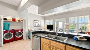 A modern kitchen with a built-in dishwasher, a double sink, and a large window with blinds. - Villagio C241 (Pensacola)