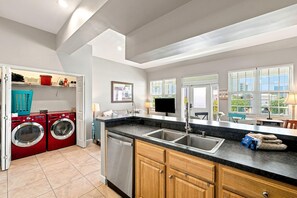 A modern kitchen with a built-in dishwasher, a double sink, and a large window with blinds. - Villagio C241 (Pensacola)
