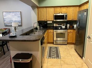 A kitchen with wooden cabinets, stainless steel appliances, a microwave, an oven, and a refrigerator. - Villagio C241 (Pensacola)