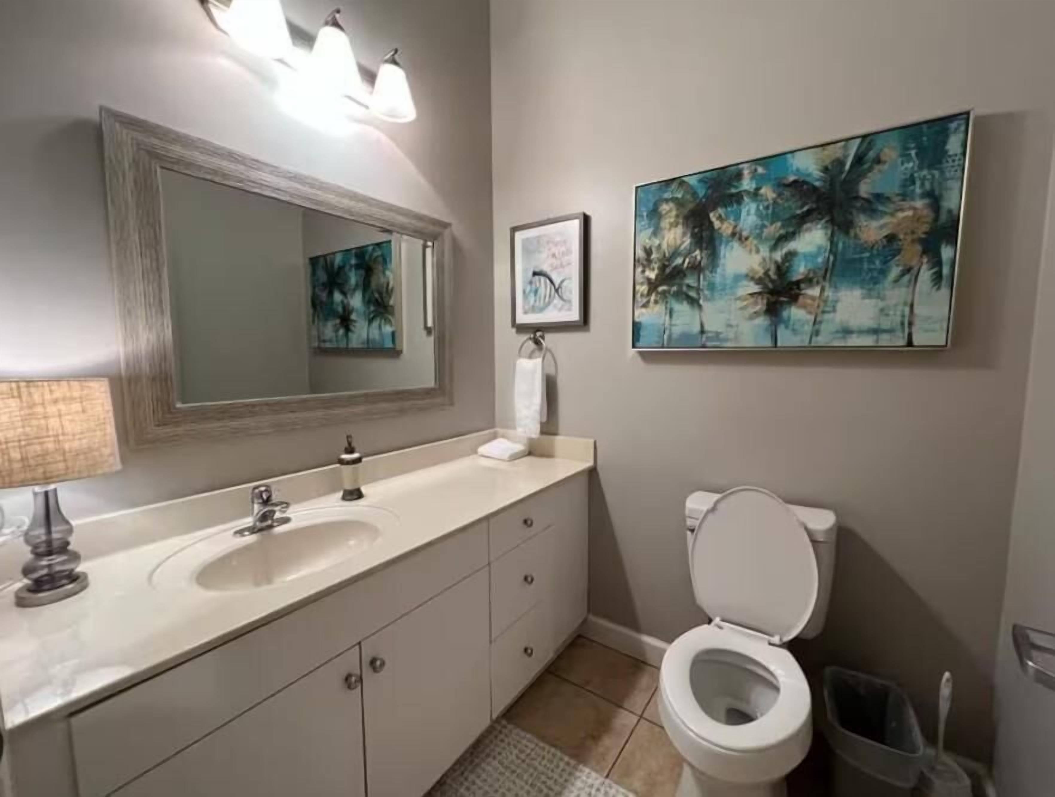 A bathroom with a sink, mirror, toilet, and a painting on the wall.