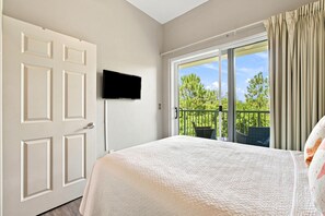 A hotel room with a bed, a television, a balcony with a view of trees, and a door. - Villagio C241 (Pensacola)