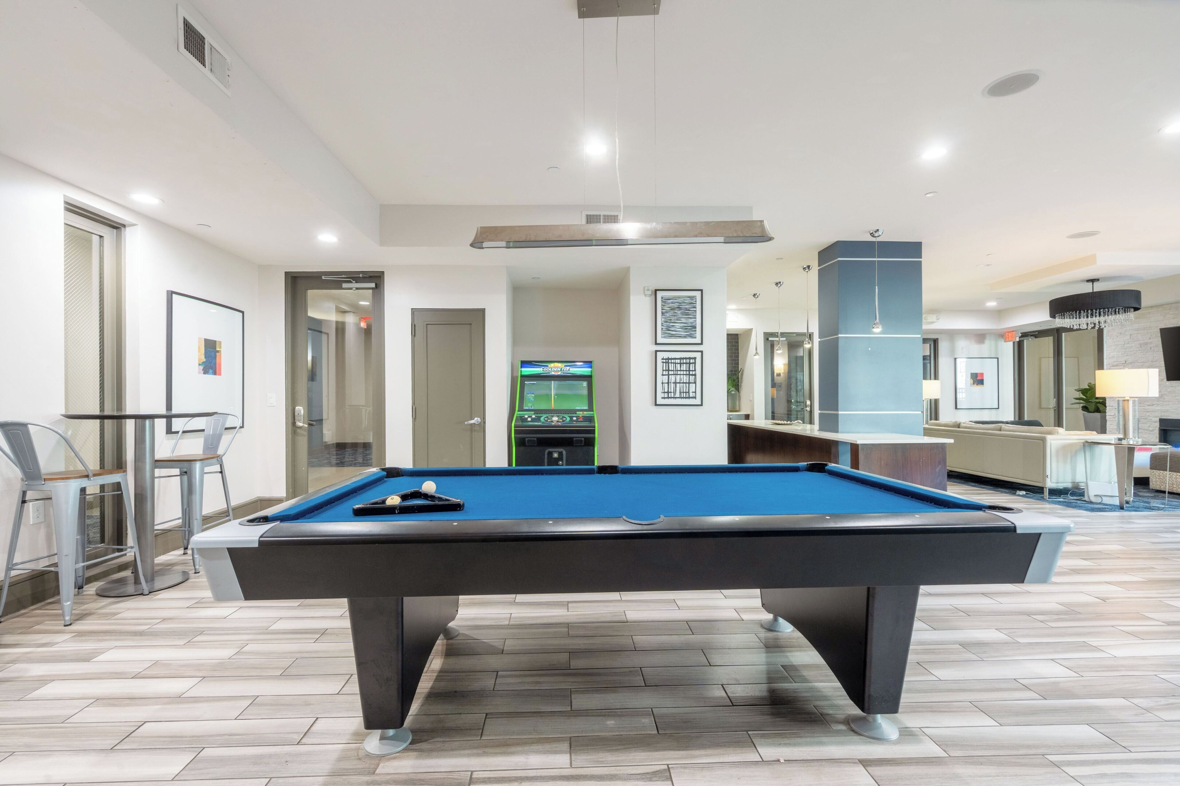 A pool table in a room with a bar area, chairs, and a door leading to another space.