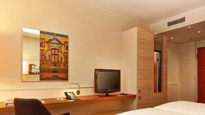 A hotel room with a bed, a desk with a computer, a chair, a painting on the wall, and a door. - 2 Person Holiday Park Home in Hannover (Hannover)