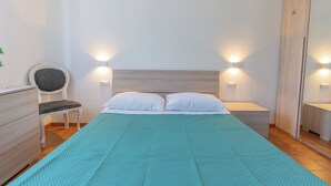 A bedroom with a bed, two bedside tables, a chair, a dresser, and wall-mounted lights.