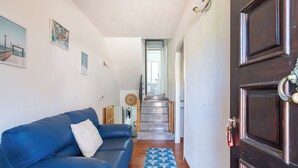 A hallway with a blue sofa, a patterned rug, a wooden staircase, and a dark wooden door.