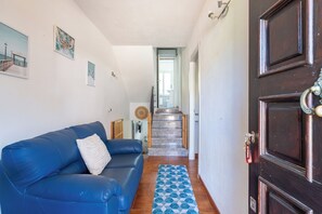 Un pasillo con un sofá azul, un tapete estampado, una escalera de madera y una puerta de madera oscura.