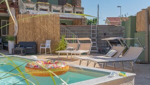 A pool area with lounge chairs, a floating ring, and a bamboo wall.