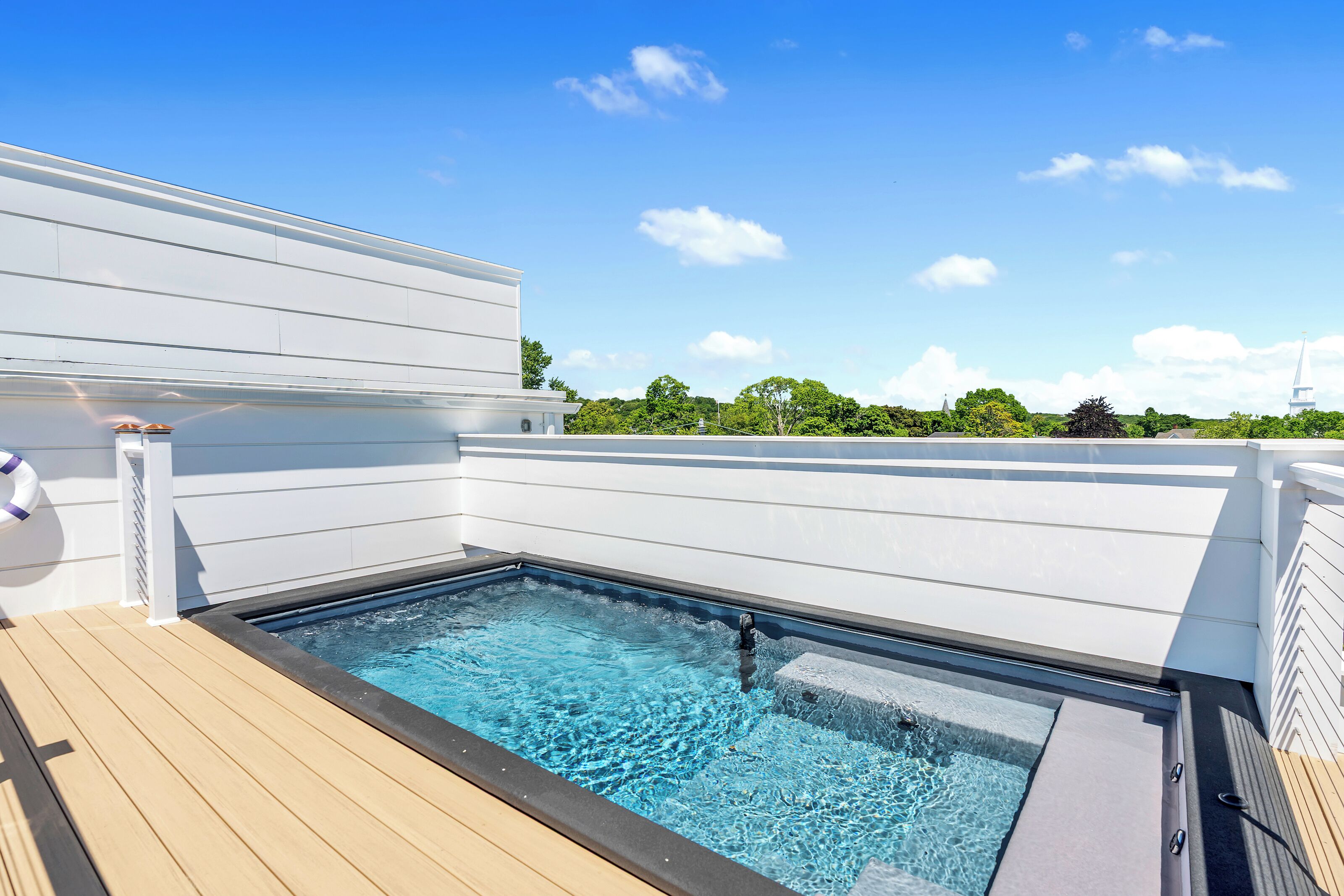 Una piscina sul tetto con un pontile in legno, pareti bianche e un cielo azzurro limpido.