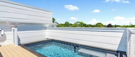 Una piscina sul tetto con un pontile in legno, pareti bianche e un cielo azzurro limpido.