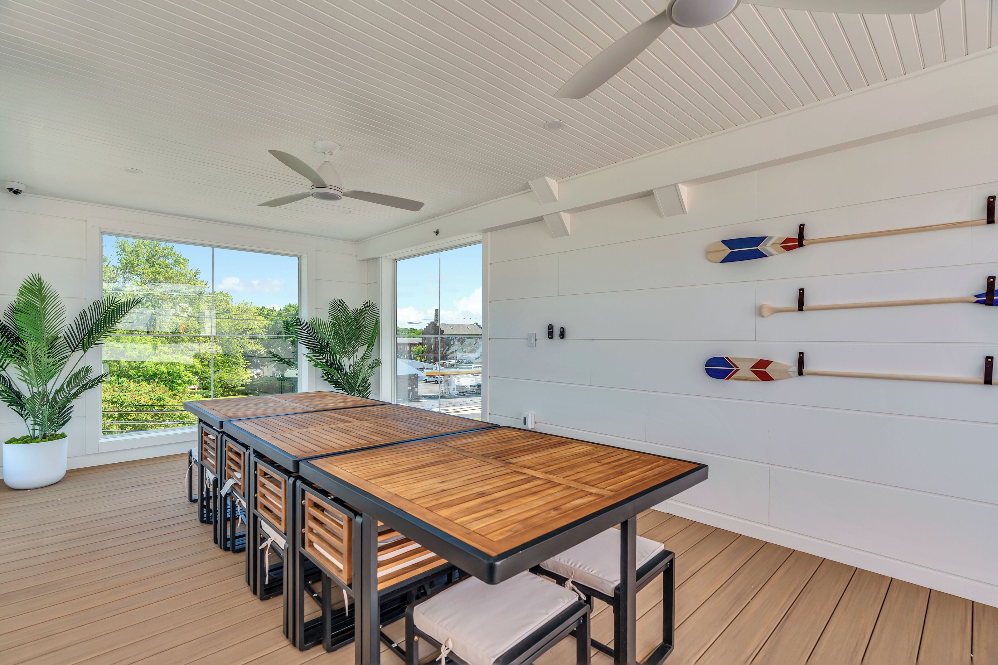 Una habitación moderna con una mesa de madera, ventiladores de techo y plantas en macetas.