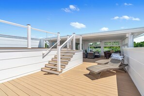 Una terraza de madera con escaleras, mobiliario exterior y un área cubierta con mesa y sillas.