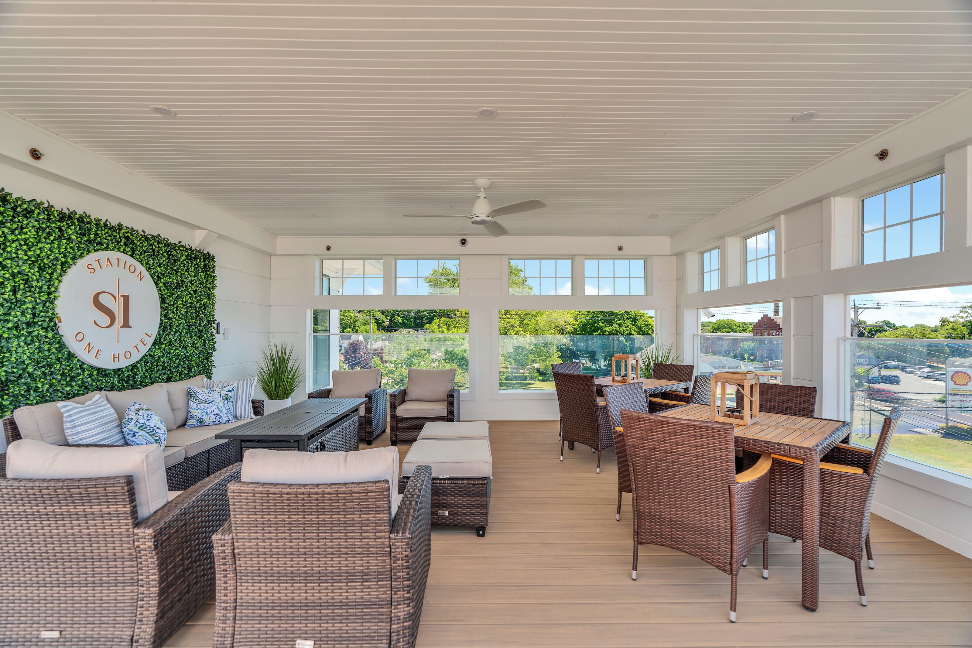 A spacious outdoor lounge area with wicker furniture, a ceiling fan, and a view of the surrounding landscape.