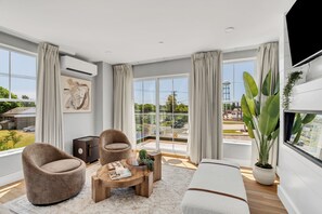 A modern living room with a sofa, two armchairs, a coffee table, and a large window with curtains. - Station 1 Hotel #3 (Stonington)