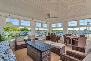 A covered outdoor seating area with wicker furniture and a table, large windows offering views of the surrounding landscape. - Station 1 Hotel #3 (Stonington)