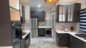 Eine moderne Küche mit dunklen Schränken, einem eingebauten Backofen, einer Waschmaschine und einer Pendelleuchte.