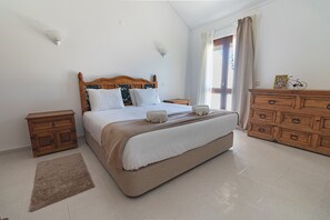 A bedroom with a bed, wooden nightstands, a dresser, a rug, and a window with curtains. - Apartamento Vintage | 4 bedrooms | Vilamoura Marina (Vilamoura)