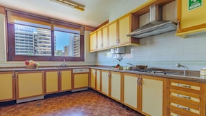 A kitchen with wooden cabinets, a window with a view of a building, and a sink. - Apartamento Vintage | 4 bedrooms | Vilamoura Marina (Vilamoura)