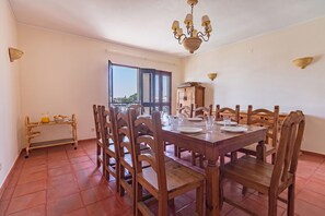 Un'area pranzo con un tavolo di legno apparecchiato per quattro persone, circondata da sedie, un lampadario e vista attraverso un'ampia finestra.