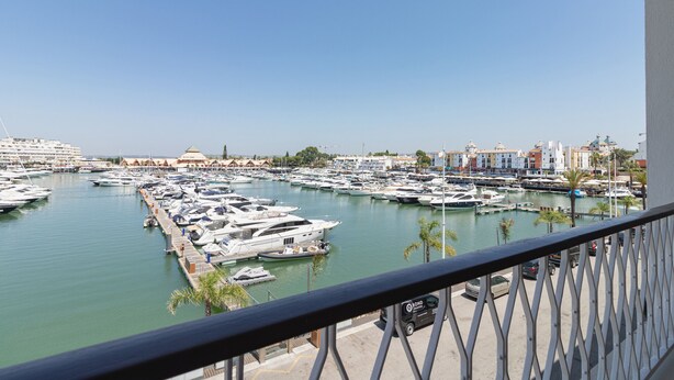 A marina with numerous boats docked, a clear sky, and buildings in the background. - Apartamento Vintage | 4 bedrooms | Vilamoura Marina (Vilamoura)