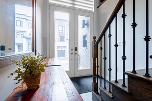 Un banc en bois avec un pot de fleurs, un escalier avec des balustrades noires et une vue sur les bâtiments environnants à travers des portes vitrées.