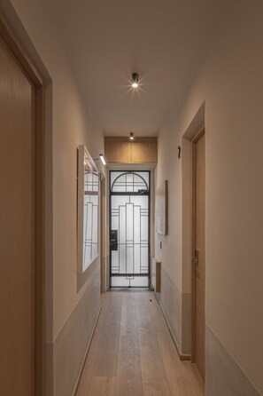 Un couloir avec une porte au fond, un luminaire au plafond et un tableau encadré au mur.